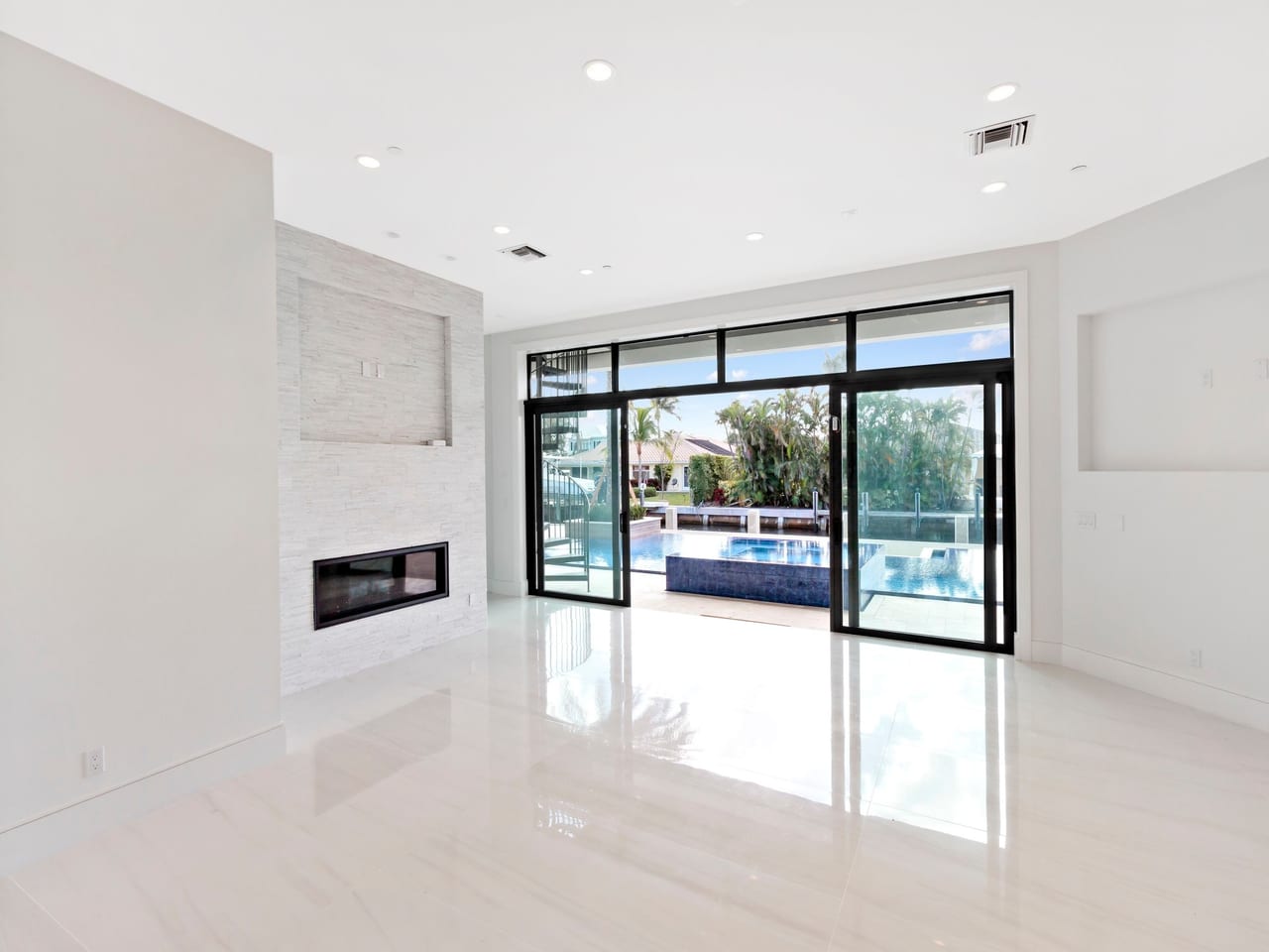 A living room opening onto a pool deck through wide impact sliding glass doors